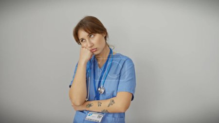 Téléchargez les photos : Jeune femme pensive en blouse bleue avec stéthoscope sur fond blanc dépeignant un professionnel de santé réfléchi. - en image libre de droit