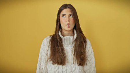 Photo for A playful young woman wearing a white sweater makes a fish face against a vibrant yellow background. - Royalty Free Image
