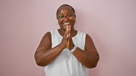 Téléchargez les photos : Femme afro-américaine confiante avec des tresses, priant les mains ensemble et souriant sur un fond rose isolé, affichant une expression joyeuse - en image libre de droit