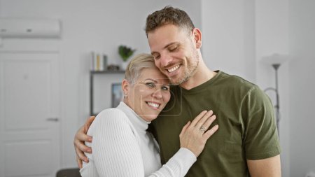 Foto de Una mujer y un hombre felices abrazándose afectuosamente en una moderna y acogedora sala de estar, retratando a una pareja amorosa en casa. - Imagen libre de derechos