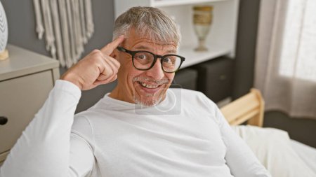 Téléchargez les photos : Homme âgé avec des lunettes dans une chemise blanche pointant sa tête, souriant dans un cadre de chambre. - en image libre de droit