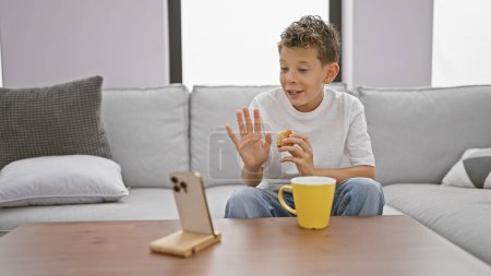 Photo for Adorable blond boy seriously engaged in online conversation, using mobile technology to eat breakfast and make video call from the cozy comfort of his living room sofa - Royalty Free Image
