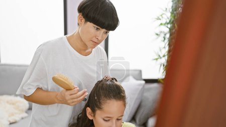 At home, heartwarming expression as mother and daughter bond, combing hair and looking at each other in the mirror in the cozy living room