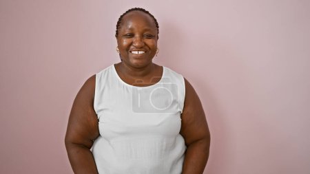 Téléchargez les photos : Femme afro-américaine confiante souriante et debout sur un fond rose isolé - en image libre de droit