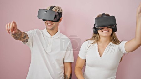 Photo for Beautiful couple playing video game using virtual reality glasses over isolated pink background - Royalty Free Image