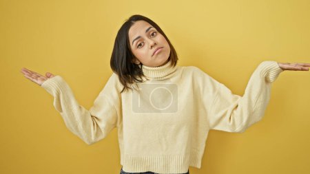 Photo for A perplexed young hispanic woman shrugs against a yellow background, showing uncertainty and emotion. - Royalty Free Image