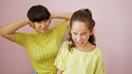 Mother and daughter, two cool family members, looking louder as they scream, covering their ears over an isolated pink background. a noisy lifestyle, expressing love through unique casual expressions.