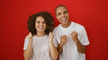 Joyful, confident couple celebrating their love, standing and smiling together over isolated red background, radiating positive aura and casual coolness