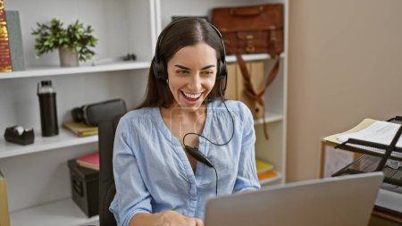 Photo for Glowing young hispanic woman is the picture of success in business - effortlessly juggles work, smiling during a video call at her office - Royalty Free Image