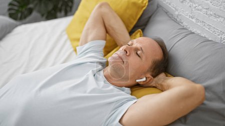 Photo for Middle age man listening to music lying on bed at bedroom - Royalty Free Image