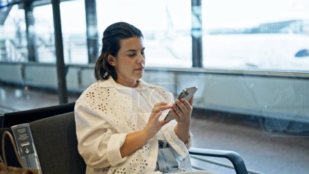 Téléchargez les photos : Belle jeune femme hispanique utilisant un smartphone à l'aéroport - en image libre de droit