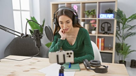 Eine fokussierte Frau sitzt beim Podcasting in einem modernen Radiostudio und trägt Kopfhörer in der Nähe eines "on air" -Schildes.