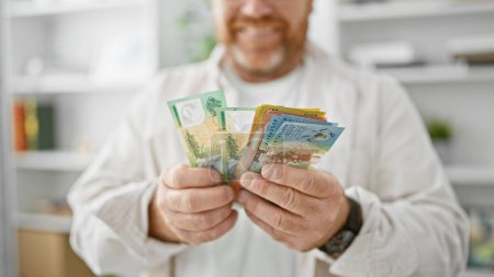 Hombre de negocios caucásico alegre con confianza contando dólares australianos en la oficina, irradiando éxito y felicidad