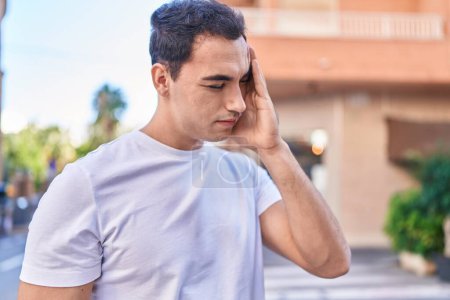 Téléchargez les photos : Jeune homme hispanique souligné souffrance pour maux de tête dans la rue - en image libre de droit
