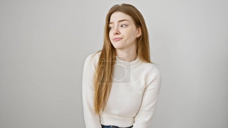 Téléchargez les photos : Portrait d'une jeune femme sceptique aux longs cheveux blonds, portant un pull blanc sur un fond blanc isolé. - en image libre de droit