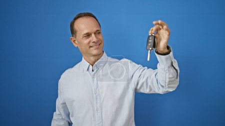 Téléchargez les photos : Homme confiant d'âge moyen tenant une nouvelle clé de voiture, souriant de joie sur fond blanc isolé - en image libre de droit
