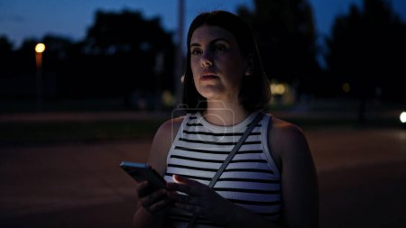 Téléchargez les photos : Jeune belle femme hispanique utilisant un smartphone dans les rues la nuit - en image libre de droit