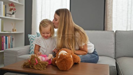 Photo for Caucasian mother and daughter happily enjoying relaxing moments at home, playfully kissing while sitting comfortably indoors, surrounded by toys - Royalty Free Image