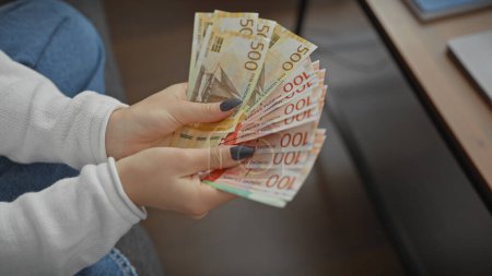 Téléchargez les photos : Une jeune femme caucasienne compte l'argent de la couronne norvégienne à l'intérieur, dépeignant la richesse et la finance à la maison. - en image libre de droit