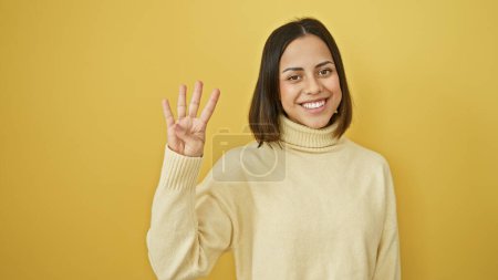 Photo for Smiling young hispanic woman posing against a yellow isolated background, cheerfully gesturing four with her hand - Royalty Free Image