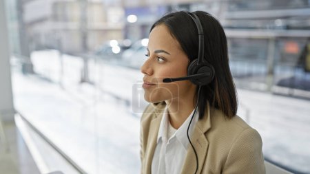 A poised young woman wearing a headset stands against a blurred indoor background, radiating professionalism.