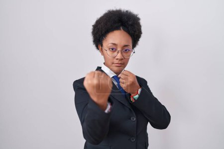 Photo for Beautiful african woman with curly hair wearing business jacket and glasses ready to fight with fist defense gesture, angry and upset face, afraid of problem - Royalty Free Image