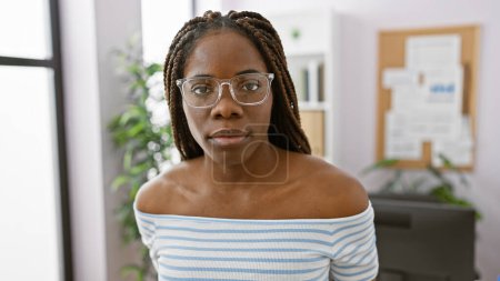 Photo for Confident african american woman with braids wearing glasses at her workplace, embodying professionalism and style. - Royalty Free Image
