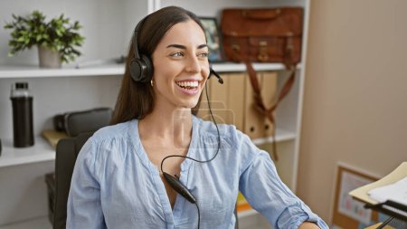 Téléchargez les photos : Une jeune femme hispanique souriante rayonne de confiance alors qu'elle gère son travail d'affaires avec joie, écoutant de la musique à travers son élégant bureau. - en image libre de droit