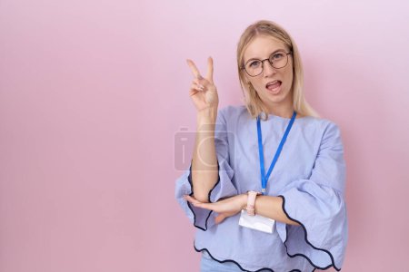 Téléchargez les photos : Jeune femme d'affaires caucasienne portant la carte d'identité souriant avec le visage heureux clin d'oeil à la caméra faisant signe de victoire avec les doigts. numéro deux. - en image libre de droit