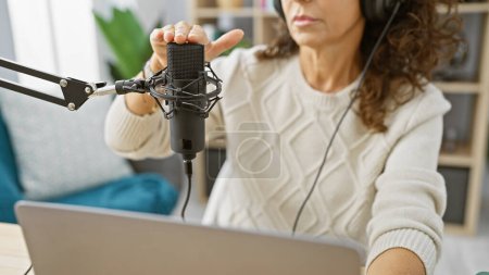 A middle-aged woman adjusts a microphone in a radio studio while working on a podcast.