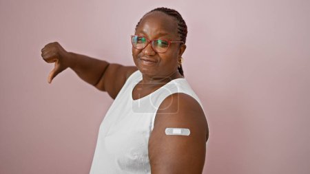 Foto de Mujer afroamericana con brazo banda de ayuda parpadea el pulgar hacia abajo signo sobre fondo rosa sereno - Imagen libre de derechos