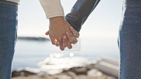 Couple holding hands at the seaside signifies love and connection amidst a beautiful ocean backdrop.