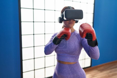 Foto de Mujer hispana hermosa joven usando gafas de realidad virtual boxeo en el centro deportivo - Imagen libre de derechos