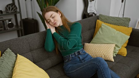 A serene young woman relaxes with closed eyes on a cozy sofa surrounded by colorful cushions in a stylish living room.