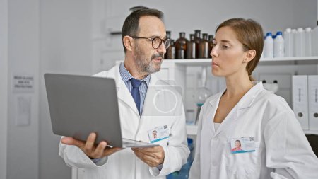Photo for Two dedicated scientists working shoulder-to-shoulder, speaking over lab analysis on a laptop in the heart of a bustling medical research laboratory. - Royalty Free Image