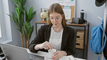 Photo for A young professional woman stirs coffee in a modern office, portraying a casual work environment. - Royalty Free Image