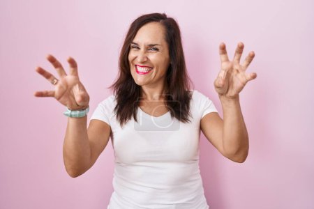 Photo for Middle age brunette woman standing over pink background smiling funny doing claw gesture as cat, aggressive and sexy expression - Royalty Free Image