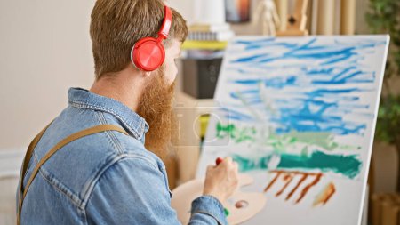 Téléchargez les photos : Passionné jeune rousse homme artiste perdu dans la musique, habilement dessin sur toile dans un atelier d'art animé - en image libre de droit