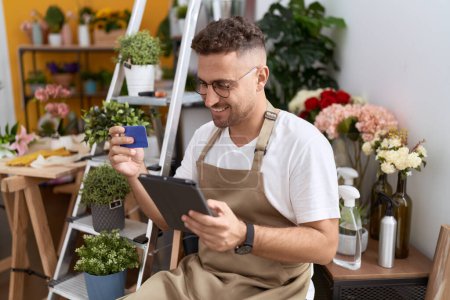 Jeune homme hispanique fleuriste en utilisant touchpad tenant carte de crédit à la boutique de fleurs