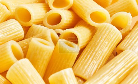 Photo for Close-up view of uncooked italian penne pasta with a textured surface and vibrant yellow hue. - Royalty Free Image
