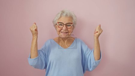 Mujer mayor alegre con pelo gris celebrando la victoria aislada sobre un fondo rosa
