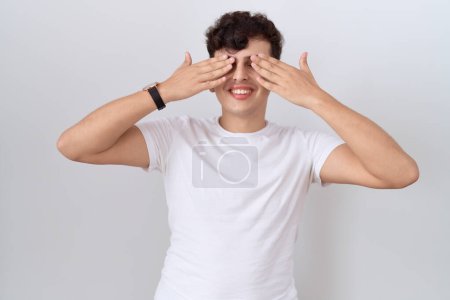 Photo for Young non binary man wearing casual white t shirt covering eyes with hands smiling cheerful and funny. blind concept. - Royalty Free Image