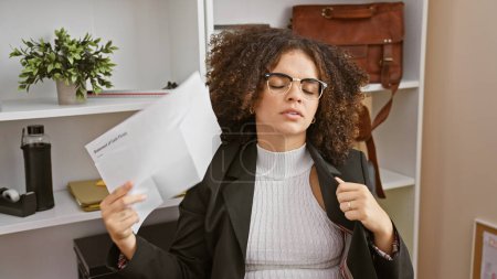 A young hispanic woman with curly hair feeling overwhelmed while reading a document in a modern office.