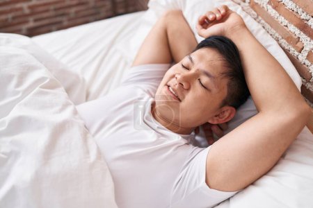 Jeune homme chinois couché sur le lit dormant dans la chambre