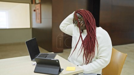 Foto de Mujer afroamericana estresada con trenzas que se siente abrumada en un entorno de oficina, retratando un desafío relacionado con el trabajo. - Imagen libre de derechos