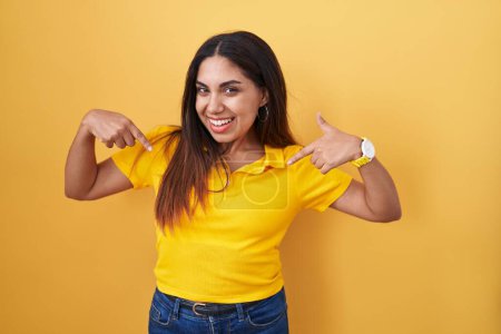 Photo for Young arab woman standing over yellow background looking confident with smile on face, pointing oneself with fingers proud and happy. - Royalty Free Image