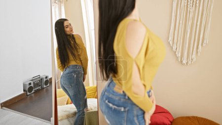 Une jeune femme hispanique dans un haut jaune et un jean pose dans une chambre confortable avec un miroir pleine longueur et une boombox jouer.