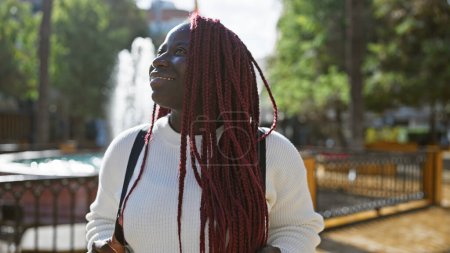 Photo for African american woman with braids smiling outdoors in a sunny city park - Royalty Free Image