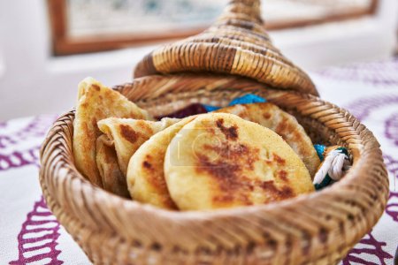 Photo for Close-up of traditional homemade corn arepas in a woven basket on a patterned tablecloth. - Royalty Free Image