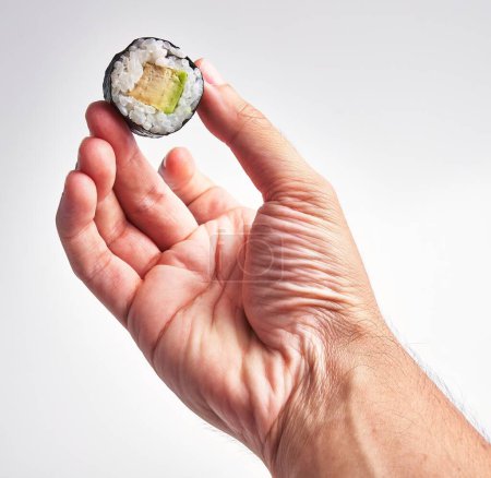 Photo for A man's hand holding a piece of sushi with cucumber and rice against a white background. - Royalty Free Image